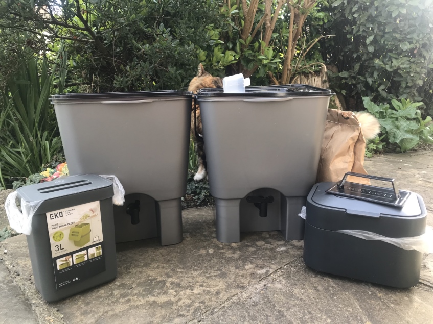 Two Bokashi bins with tops, two small food waste containers with a cat passing behind. The cat is shorter and longer than a Bokashi bin